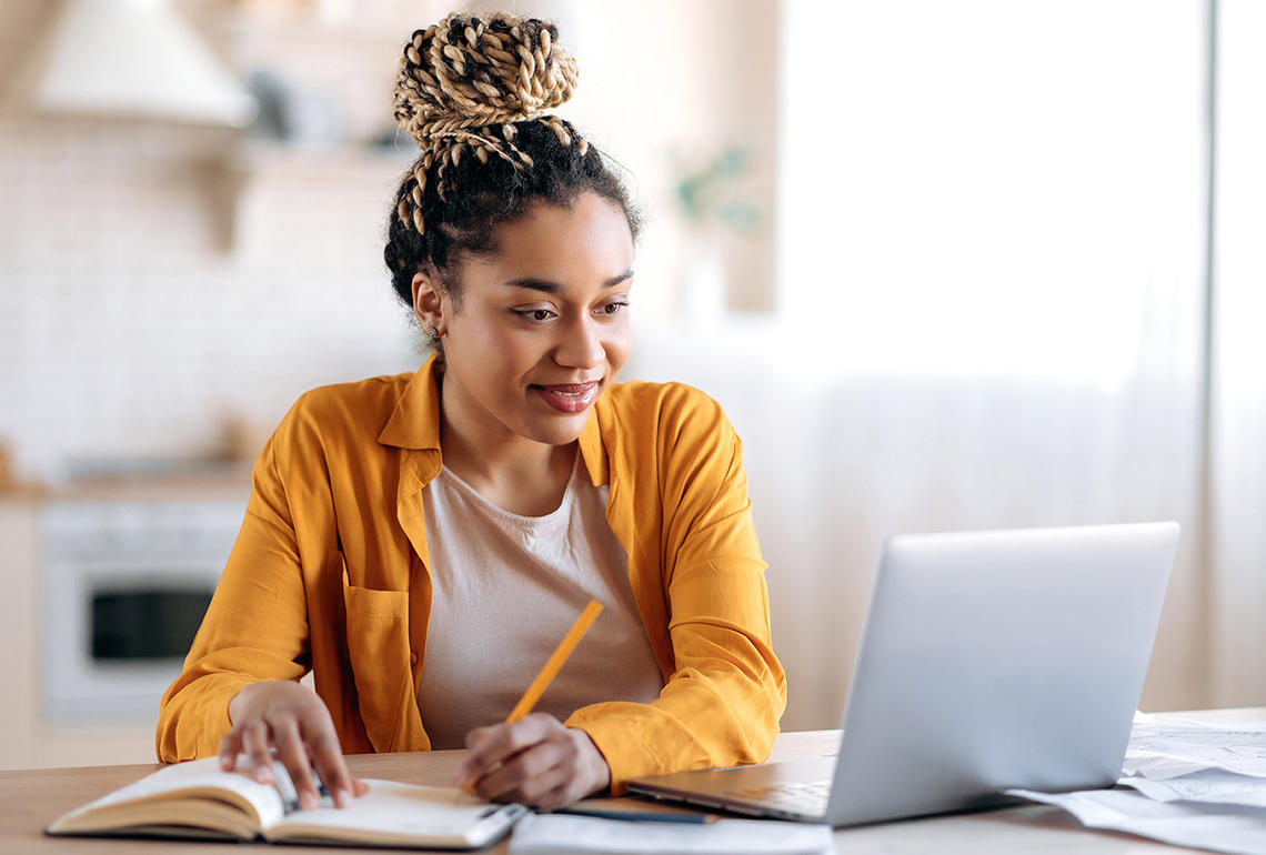 Young Black female sitting at a desk working with a laptop and an open notebook