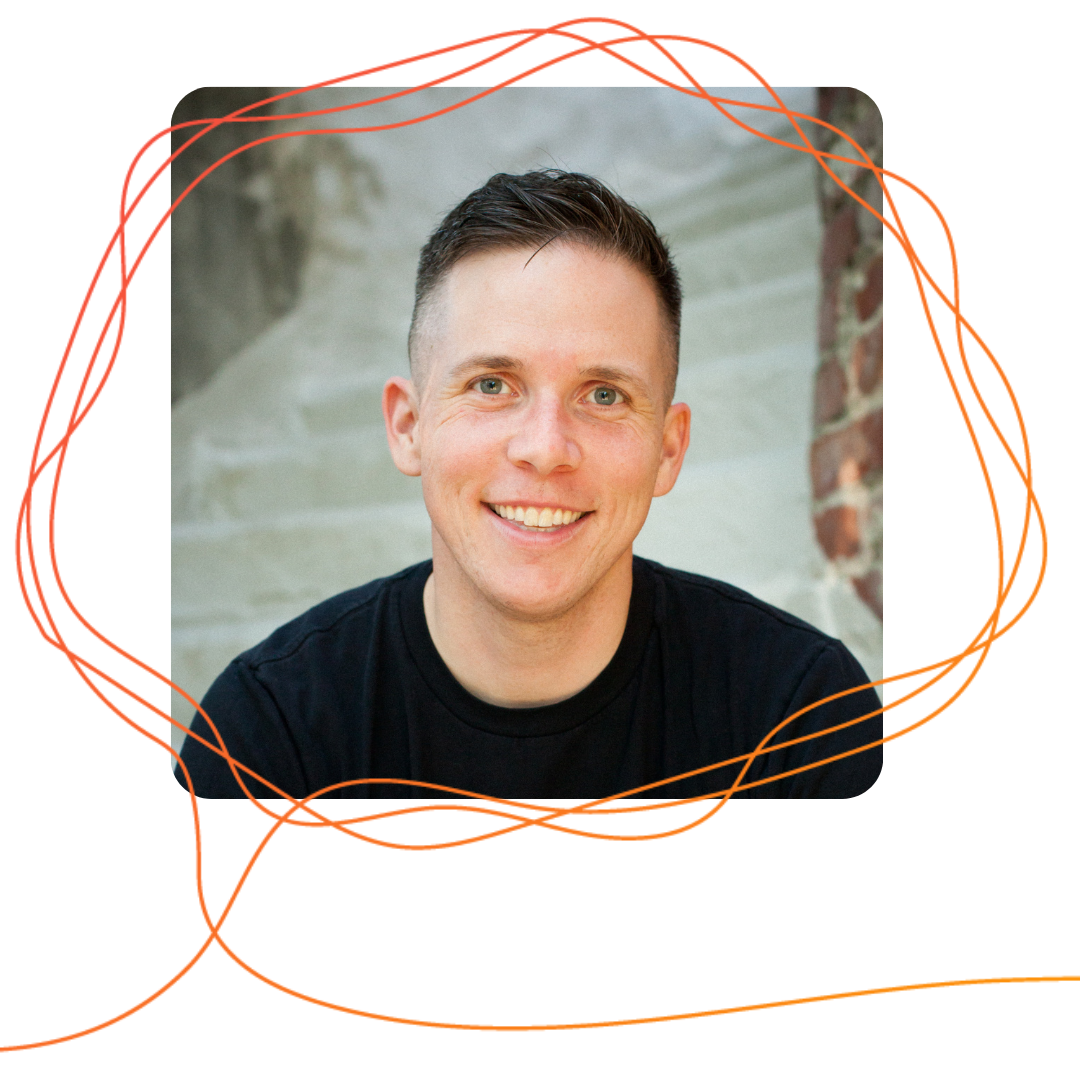 Harper Keenan, a white man with short dark hair wearing a black t-shirt, is looking ahead and smiling with a brick wall behind him.