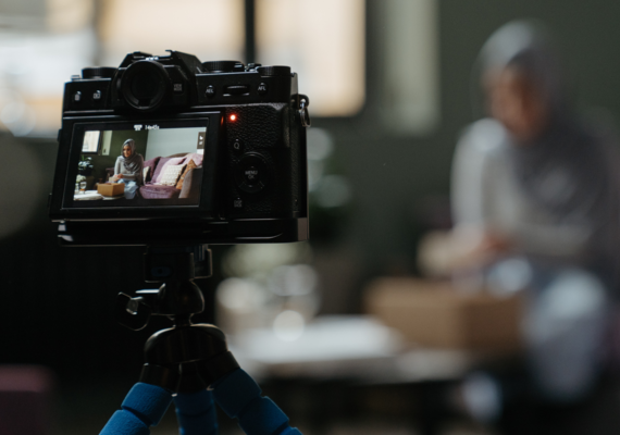 The back of a camera with a screen looking at a person wearing a hijab sitting on a couch.